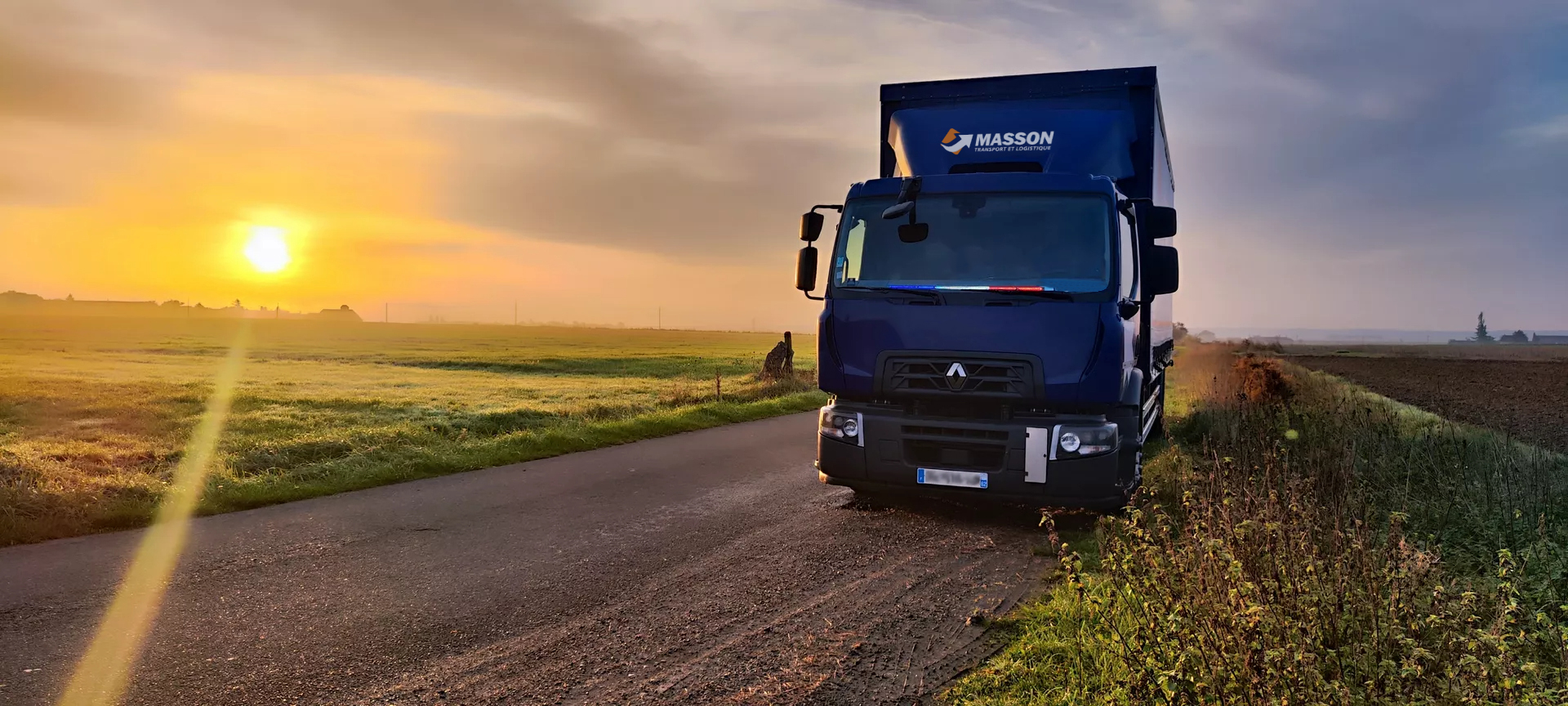 Photo représentant un camion des transport Masson sur le bord de la route au levé du soleil.